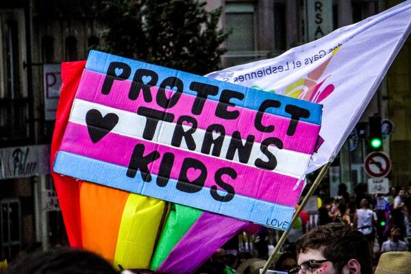 Manos sosteniendo un cartel que dice “Protect Trans Kids” durante una marcha